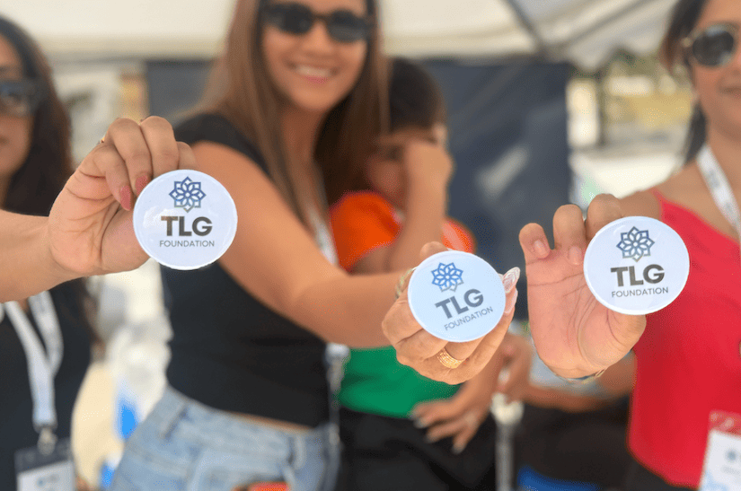 Hands holding round TLG Foundation badges at Festival Gandhi 2026