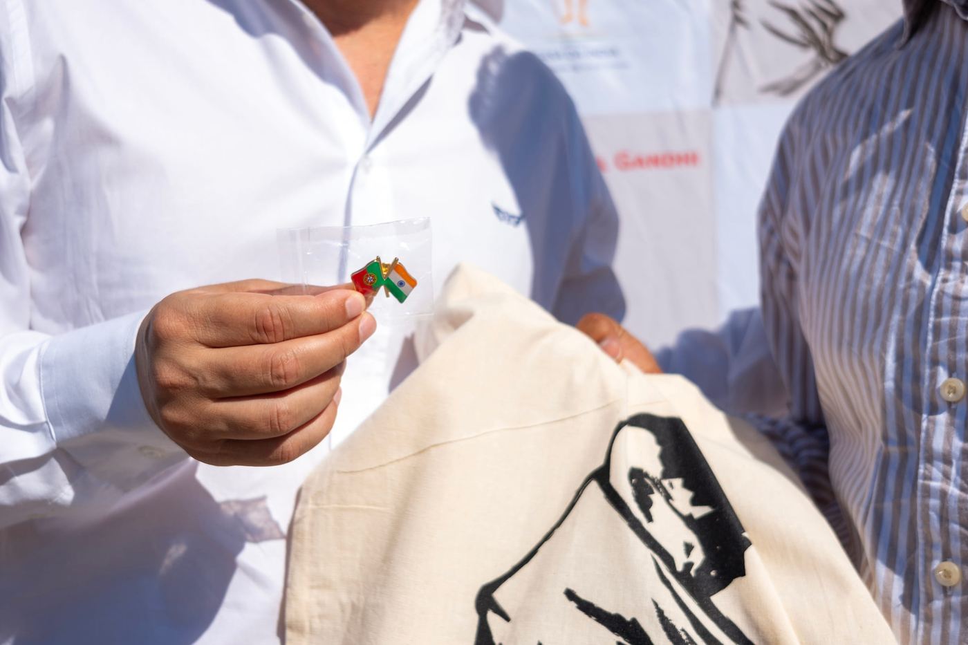 A Portugal-India friendship pin held next to a Festival Gandhi 2026 volunteer T-shirt